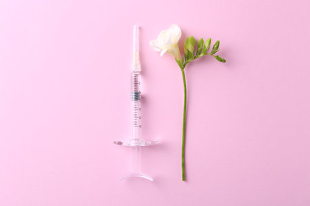 Cosmetology. Medical syringe and freesia flower on pink background, flat layの写真素材