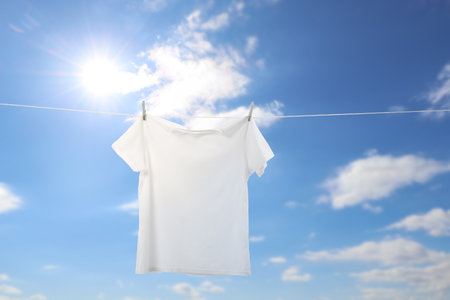 White t-shirt drying on washing line against blue skyの写真素材