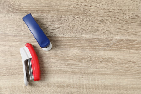 Color staplers on wooden table, flat lay. Space for text