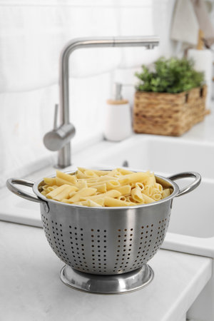Cooked pasta in metal colander on countertop near sink. Space for textの写真素材