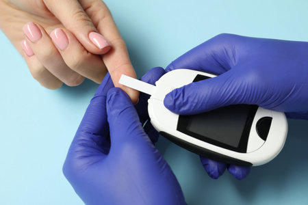 Diabetes. Doctor checking patient's blood sugar level with glucometer on light blue background, top...