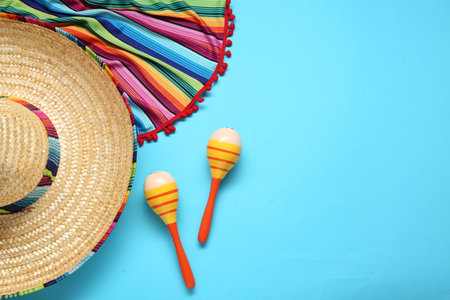 Mexican sombrero hat, maracas and colorful poncho on light blue background, flat lay. Space for textの写真素材