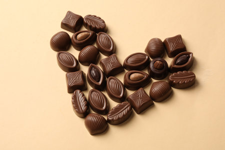 Heart made with delicious chocolate candies on beige background, above view