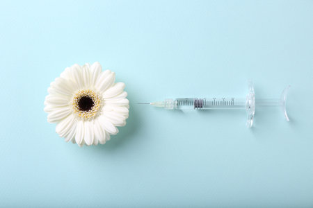Cosmetology. Medical syringe and gerbera flower on light blue background, flat layの写真素材