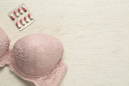 Breast cancer awareness. Bra and pills on white wooden table, flat lay. Space for textの写真素材