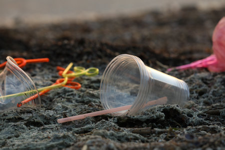 Used plastic cups and straws at beach, closeup and space for text. Environmental pollution concept