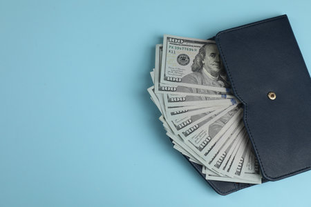 Money exchange. Wallet with dollar banknotes on light blue background, top view. Space for text