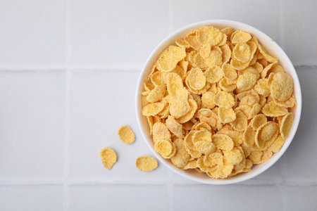 Breakfast cereal. Tasty crispy corn flakes in bowl on white tiled table, top view. Space for text