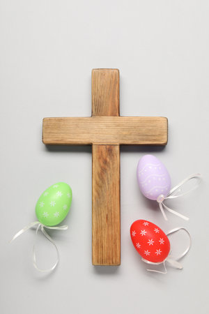 Wooden cross and painted Easter eggs on light gray background, flat layの写真素材