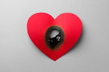 Red paper heart with burnt hole on white background, top view. Broken heartの写真素材
