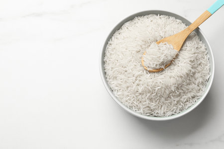 Raw basmati rice with spoon in bowl on white marble table, top view. Space for textの写真素材