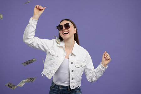 Happy woman under money shower on purple backgroundの写真素材
