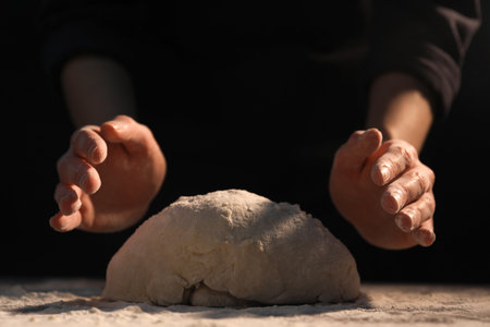 Making bread. Woman kneading dough at table on dark background, closeup