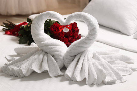 Honeymoon. Swans made of towels and beautiful red roses on bed in roomの写真素材