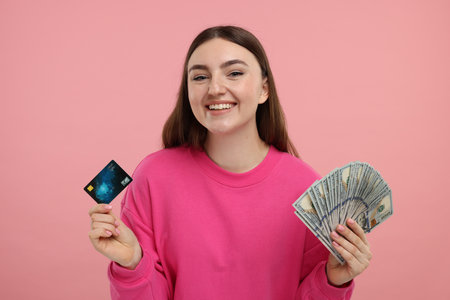 Happy woman with credit card and dollar banknotes on pink backgroundの写真素材