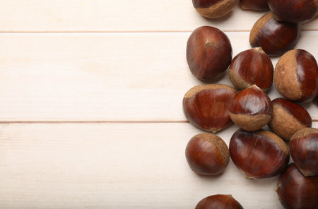 Sweet fresh edible chestnuts on light wooden table, top view. Space for textの写真素材