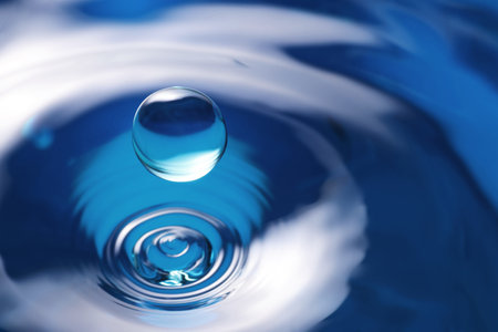 Splash of clear water with drop on blue background, closeup