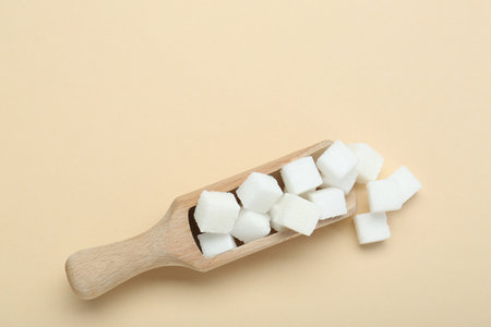 White sugar cubes and wooden scoop on beige background, top view. Space for textの写真素材