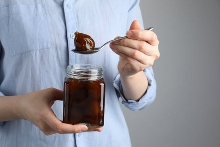 Woman holding jar of tasty sweet fig jam on gray background, closeup. Space for textの写真素材