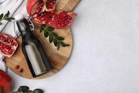 Tasty pomegranate sauce in bottle, branches and fruits on light table, flat lay. Space for textの写真素材