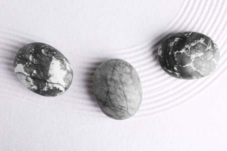 Zen garden stones on white sand with pattern, flat lay