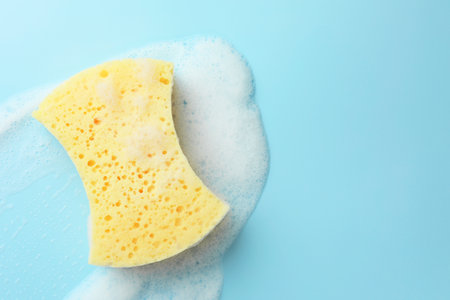 Yellow sponge with foam on light blue background, top view. Space for textの写真素材