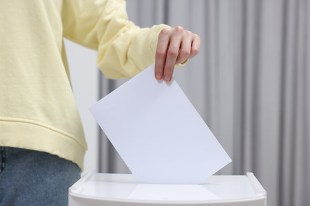 Woman putting her vote into ballot box on blurred background, closeupの写真素材