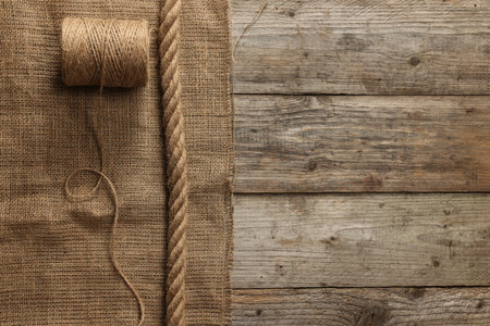 Burlap fabric, spool of thread and jute on wooden table, top view. Space for textの写真素材