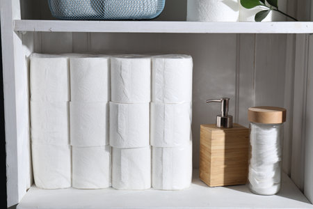 Toilet paper rolls, dispenser and cotton pads on white shelf