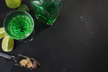 Absinthe, spoon, brown sugar and lime on black table, flat lay with space for text. Alcoholic drink