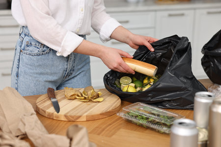 Garbage sorting. Woman putting food waste into plastic bag at wooden table indoors, closeupの写真素材
