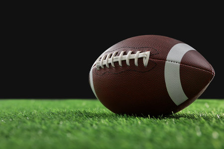 Rugby ball on green grass against black background, space for textの写真素材
