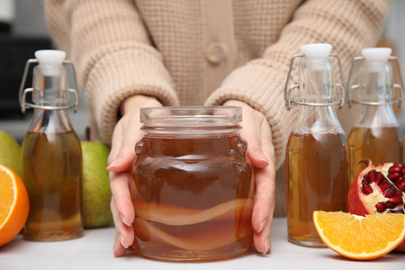 Woman taking jar of homemade fermented kombucha at white table, closeupの写真素材