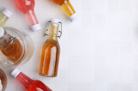 Tasty kombucha in glass bottles on white tiled table, flat lay. Space for textの写真素材