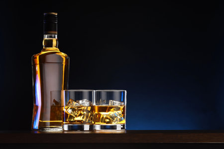 Whiskey with ice cubes in glasses and bottle on table against dark background, space for textの写真素材