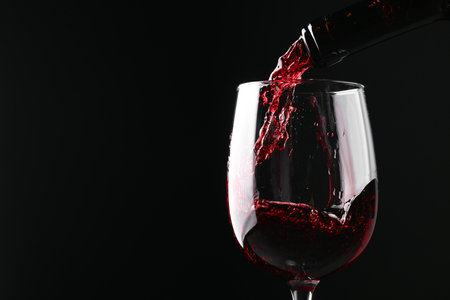 Pouring red wine into glass against black background, closeup. Space for textの写真素材