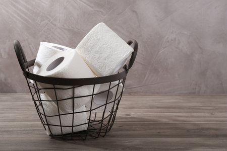 Soft toilet paper rolls in metal basket on wooden table, closeup. Space for textの写真素材