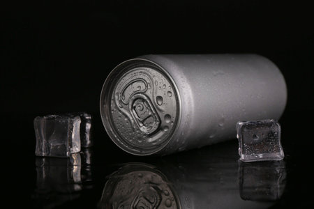 Energy drink in wet can and ice cubes on black background, closeup