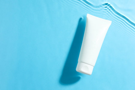 Tube with moisturizing cream in water on light blue background, top view. Space for textの写真素材