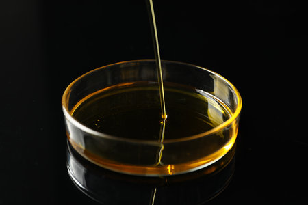 Pouring yellow oil into Petri dish on black background, closeupの写真素材