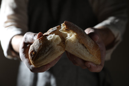 Man breaking loaf of fresh bread on dark background, closeupの写真素材