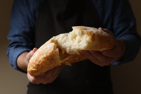 Man breaking loaf of fresh bread on dark background, closeup