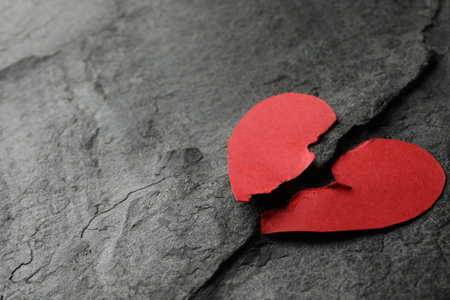 Halves of torn red paper heart on dark gray table, space for text. Broken heartの写真素材