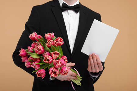 Man with beautiful bouquet and greeting card on beige background, closeupの写真素材