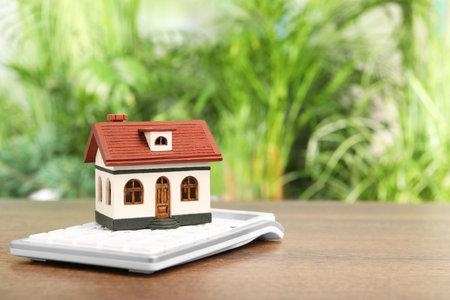 Mortgage concept. House model and calculator on wooden table against blurred green background, closeup with space for textの写真素材