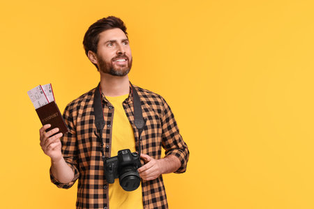 Smiling man with passport, tickets and camera on yellow background. Space for textの写真素材