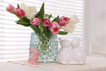 Easter decorations. Bouquet of tulips in vase and bunny figures on white table at homeの写真素材