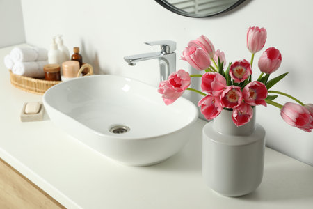 Vase with beautiful pink tulips and toiletries near sink in bathroomの写真素材