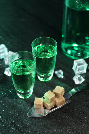 Absinthe in shot glasses, spoon, brown sugar and ice cubes on gray table. Alcoholic drink