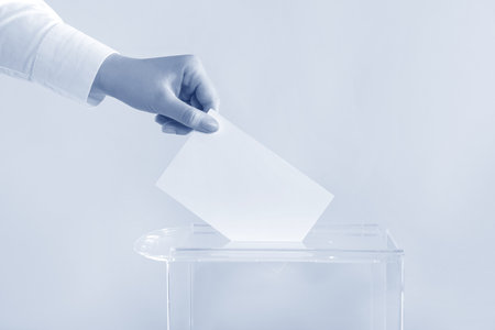 Woman putting her vote into ballot box on background, closeup. Color toned